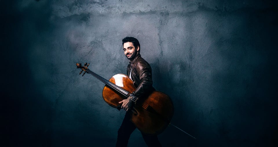 Pablo Ferrandez trägt sein Violoncello vor einem blauen Hintergrund
