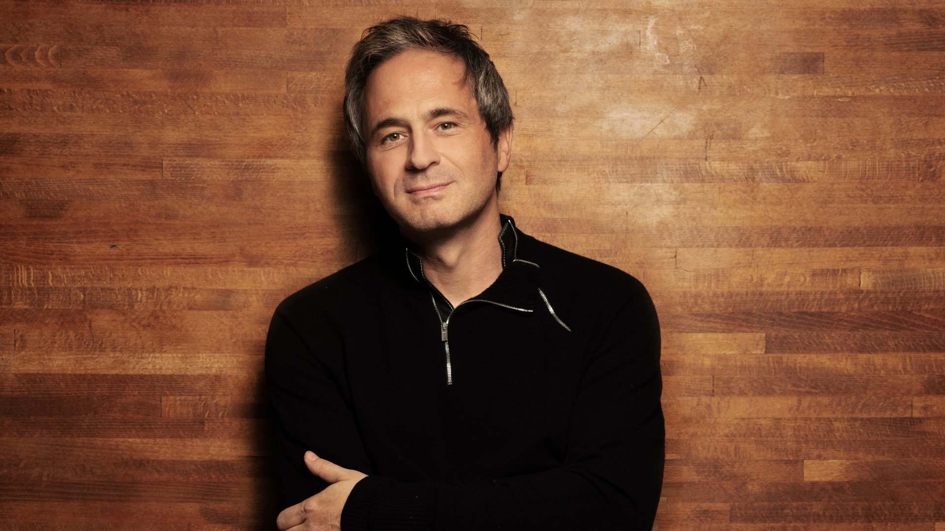 Ein Foto für die Veranstaltung ‚7. Abokonzert‘ mit dem Künstler vor einem holzfarbenen Hintergrund