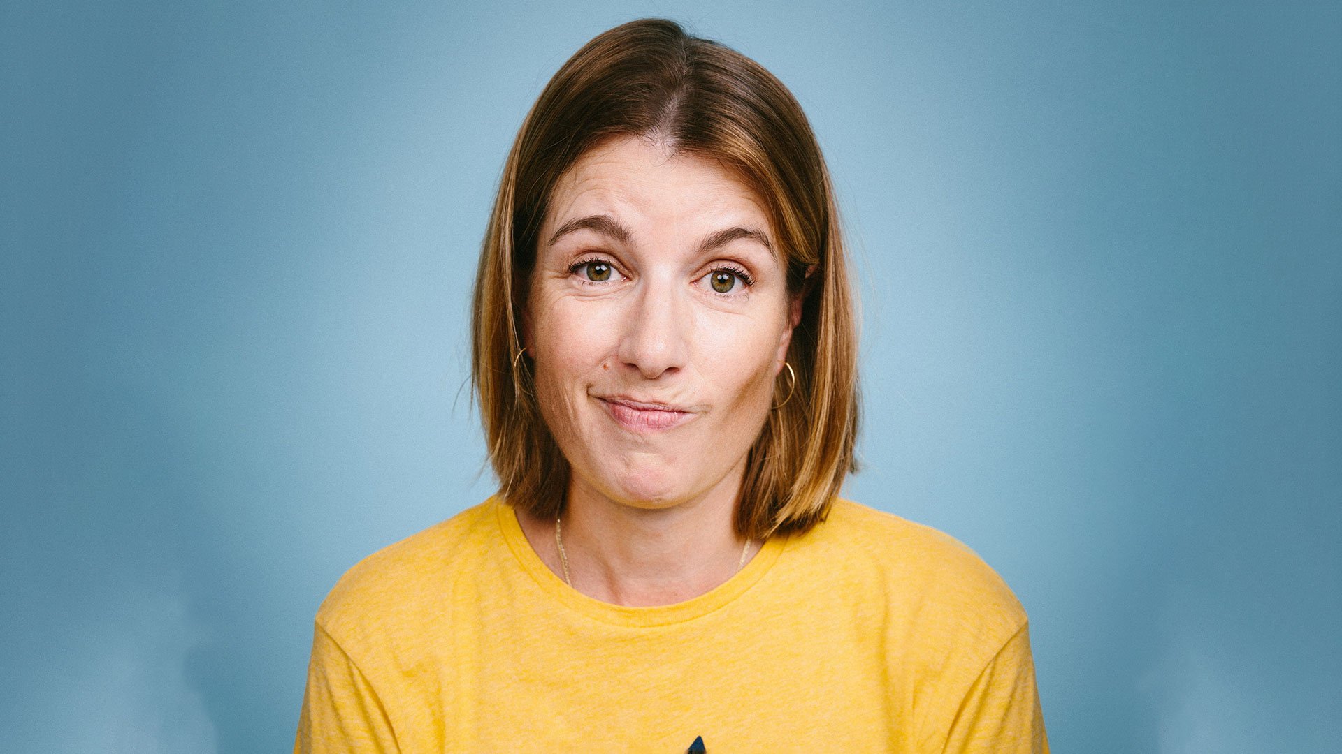 Foto für die Veranstaltung von Suse Lichtenberger mit der Künstlerin im gelben T‑Shirt vor blauem Hintergrund