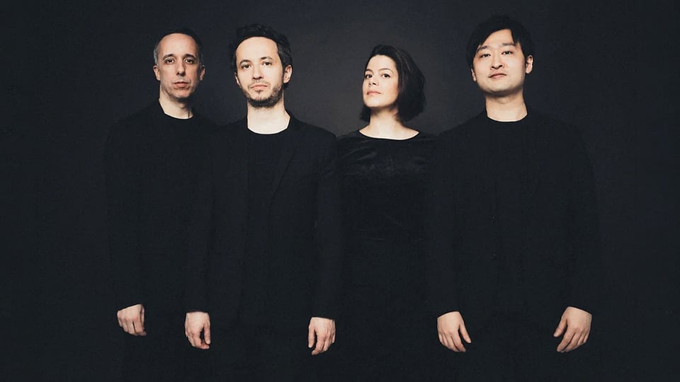 Quatuor Ébène mit vier Personen in dunkler Kleidung vor schwarzem Hintergrund, nebeneinander stehend in einer Studioaufnahme ohne sichtbare Instrumente.