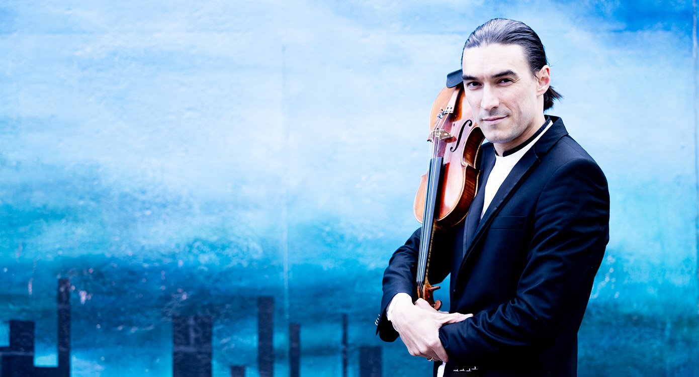 Foto von Sergey Malov mit einem Streichinstrument auf der Schulter vor blauem Hintergrund – für das Event Kammerphilharmonie Ingolstadt & Sergey Malov