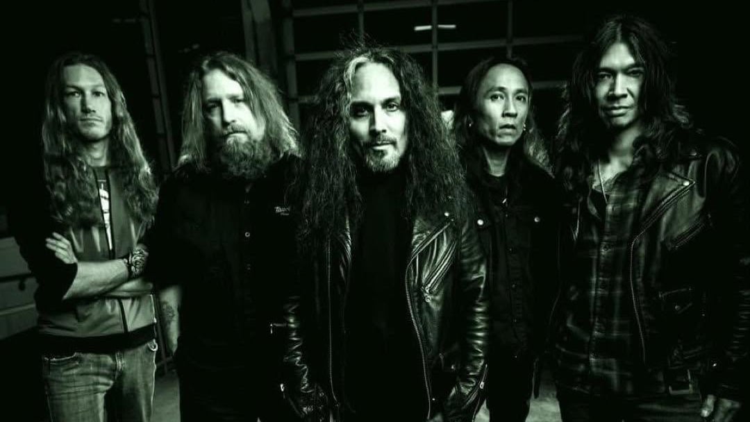 Death Angel in dunkler Kleidung posieren für ein schwarz-weißes Gruppenfoto vor einem dunklen Hintergrund.