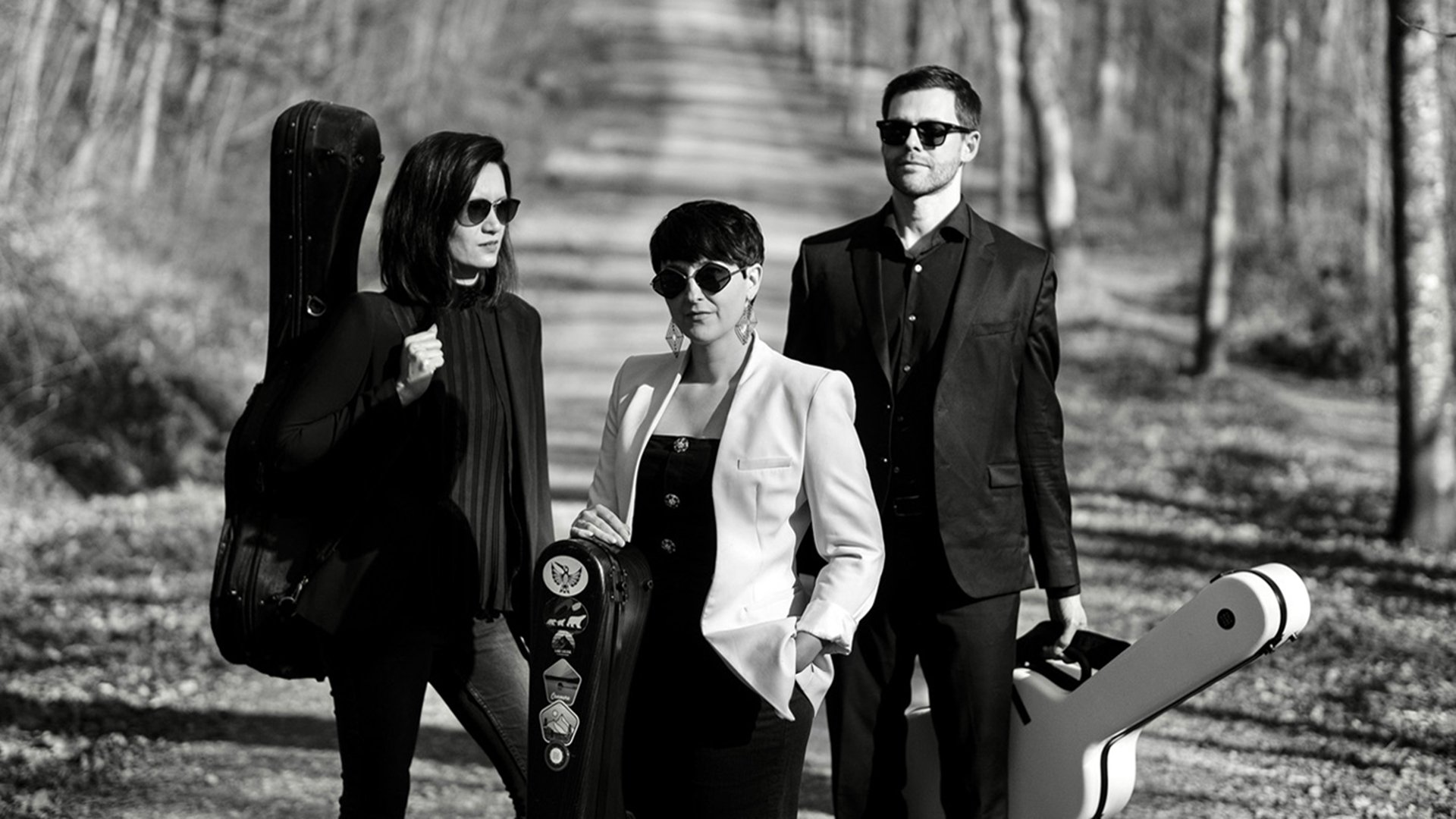 Ein schwarz-weiss Foto von drei Personen auf einem Waldweg mit Instrumentenkoffer