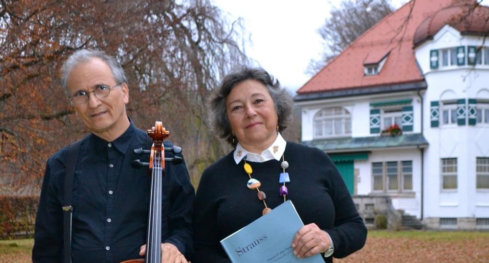 Eine Dame und ein Herr, er mit Instrument, vor einem historischen Gebäude