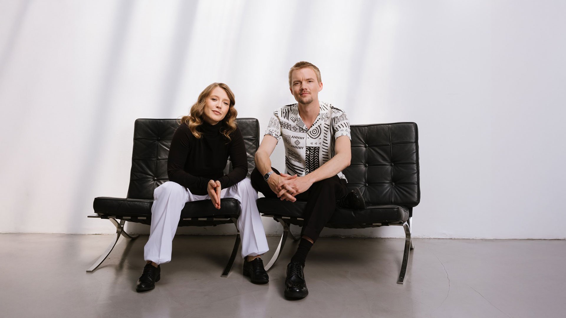 Pressefoto von Wiener Blond mit zwei Personen, die auf schwarzen Ledersesseln vor hellem Hintergrund sitzen.
