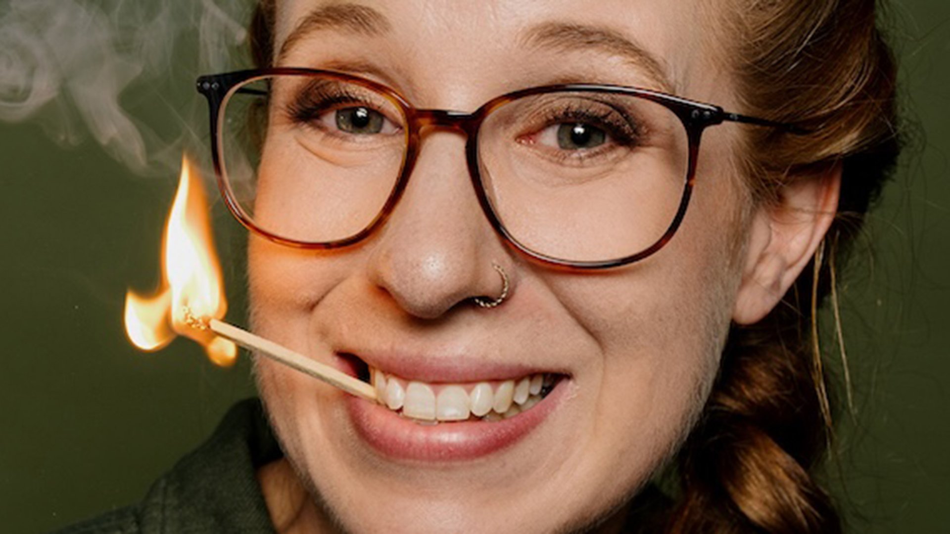 Die Künstlerin mit Brille und einem brennenden Streichholz im Mund