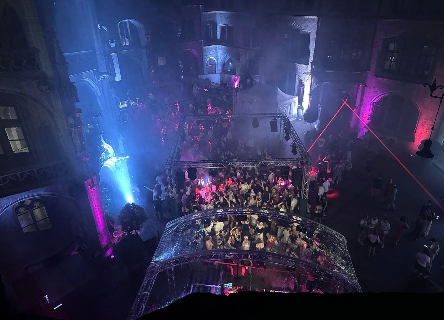 Partygesellschaft bei Nacht unter freiem Himmel auf Stadtplatz mit pinker und blauer Beleuchtung