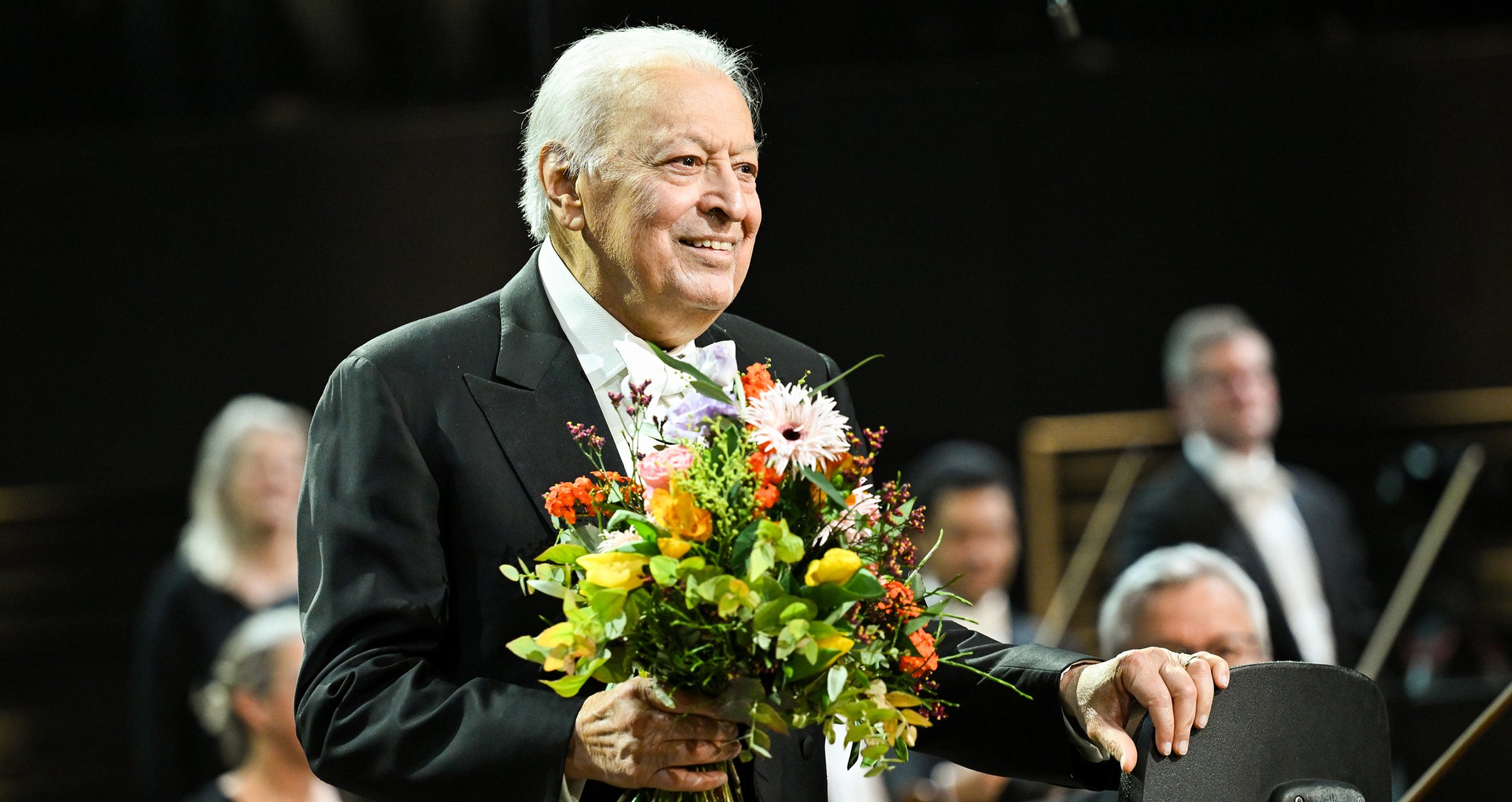 ein Mann mit einem Blumenstrauß und ein Orchester im Hintergrund