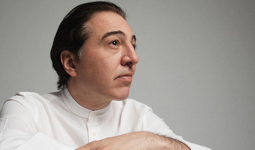 Der Künstöer Fazil Say in weißem Hemd zur Seite blickend, vor hellgrauem Hintergrund