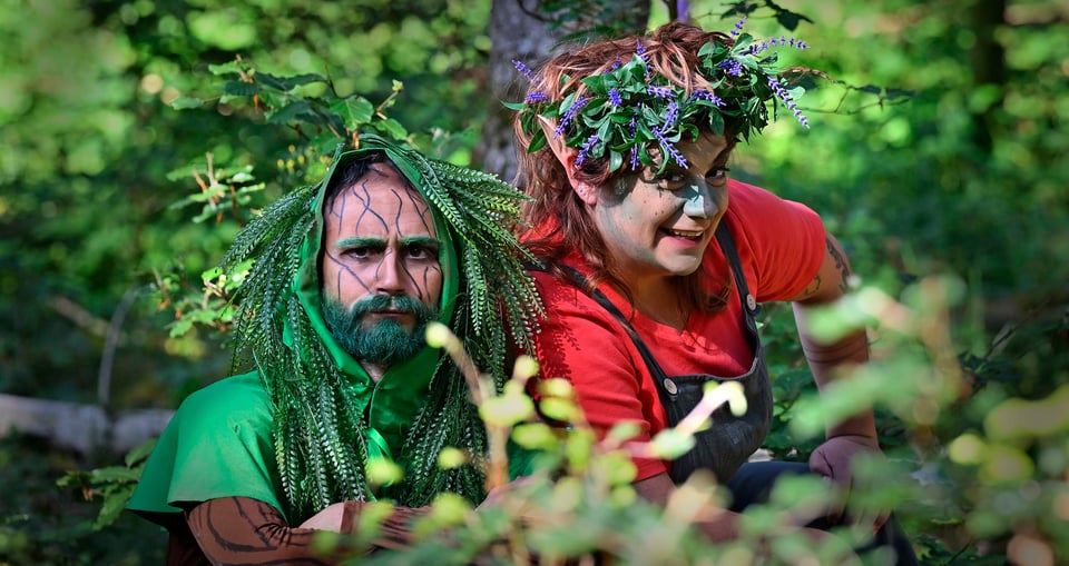 Zwei Personen mit bunter Tarnung und bunter Kleidung und Wald als Hintergrund