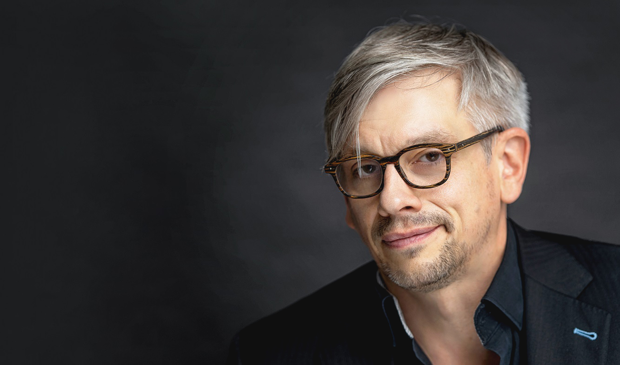 Matthias Tretter in schwarzem Hemd mit Brille vor grauem Hintergrund