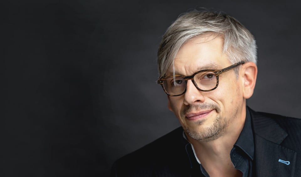 Matthias Tretter in schwarzem Hemd mit Brille vor grauem Hintergrund