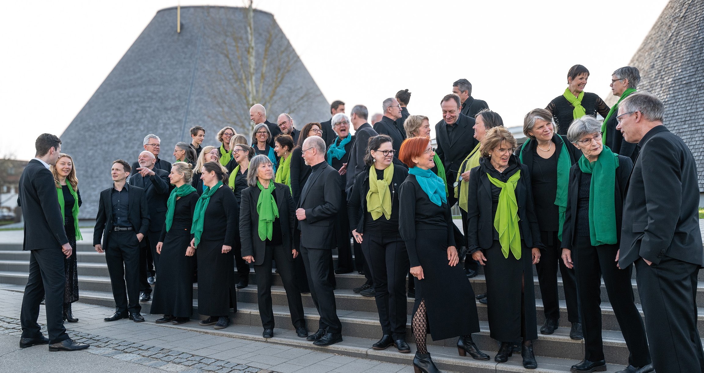 Foto einer Gruppe von Personen, alle in Schwarz gekleidet, mit Schals in Grün- und Blautönen.