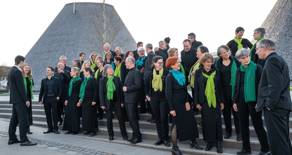 Foto einer Gruppe von Personen, alle in Schwarz gekleidet, mit Schals in Grün- und Blautönen.