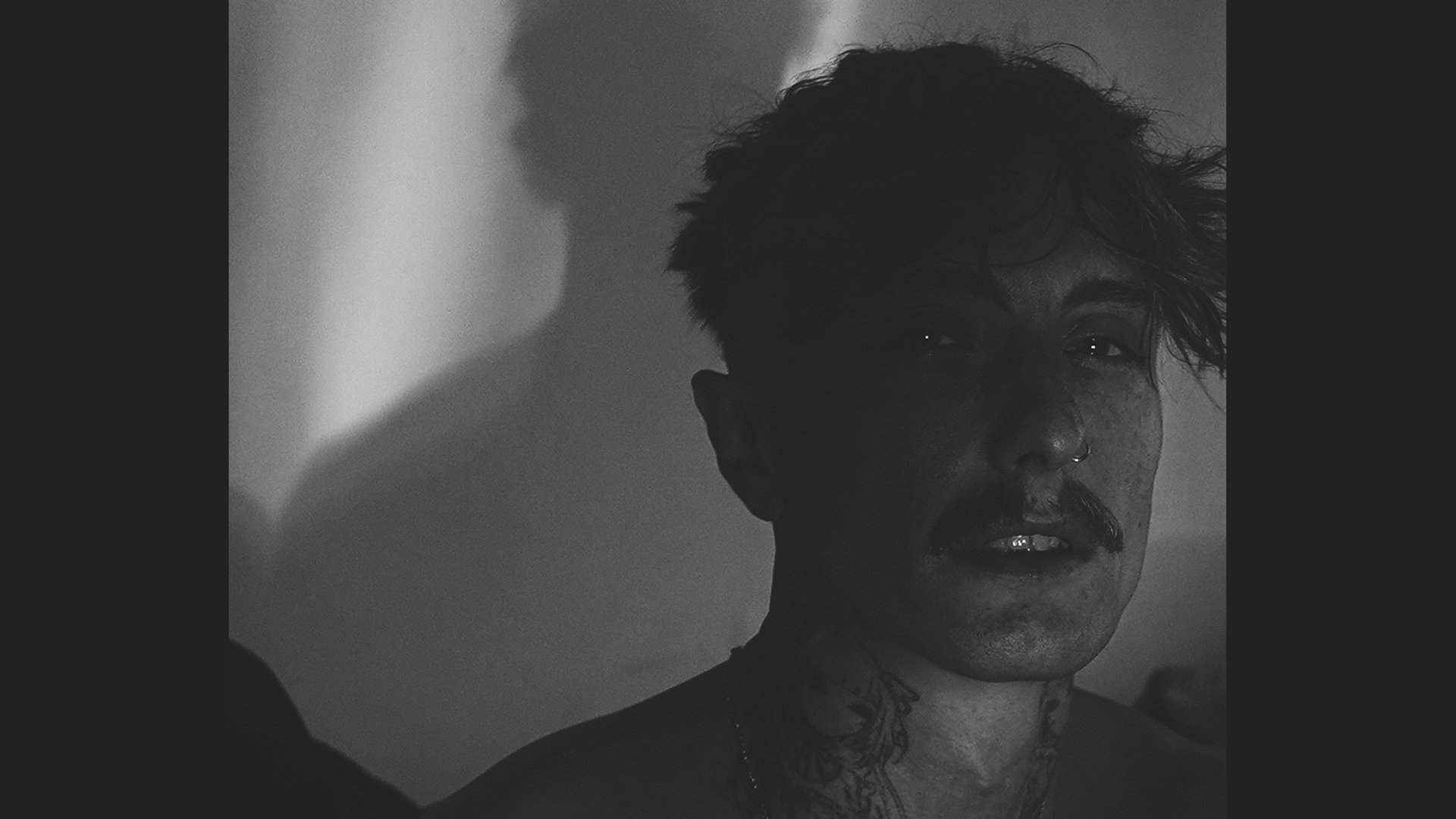 Schwarz-weiss Foto einer Person mit einem Tattoo am Hals zur Veranstaltung The haunted Youth mit Schatten im Hintergrund