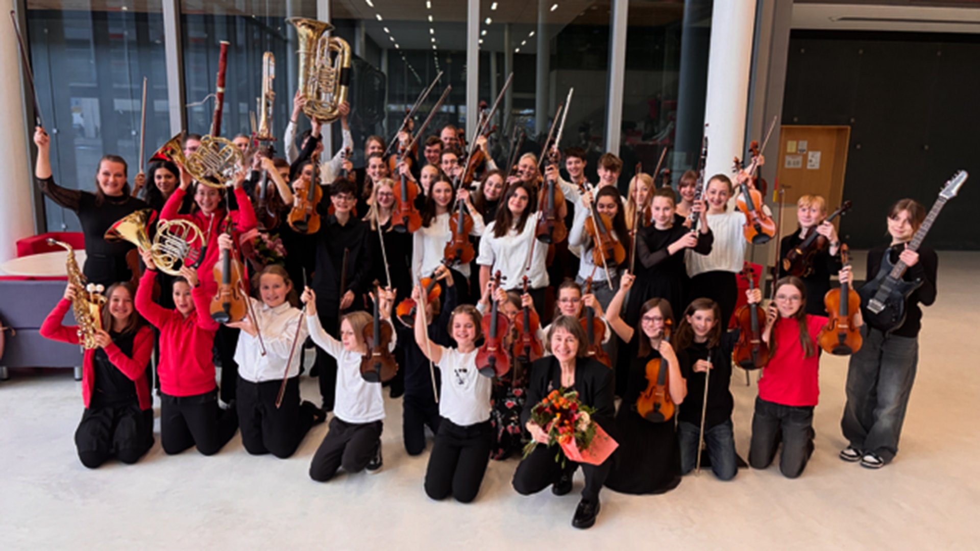Das DachauerJugendsinfonieorchester in schwarz, rot und weiss gekleidet mit Instrumenten in einer Halle