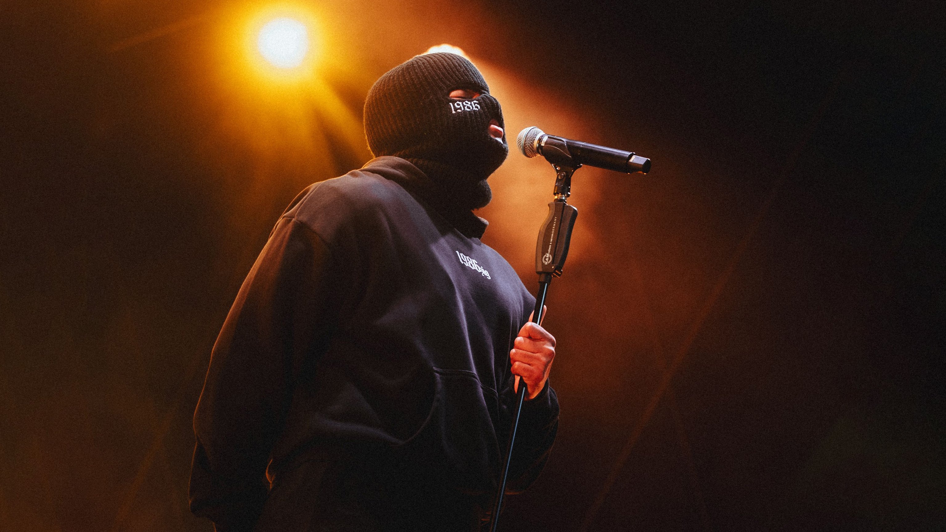 1986zig singt mit einer Sturmhaube in ein Mikrofon