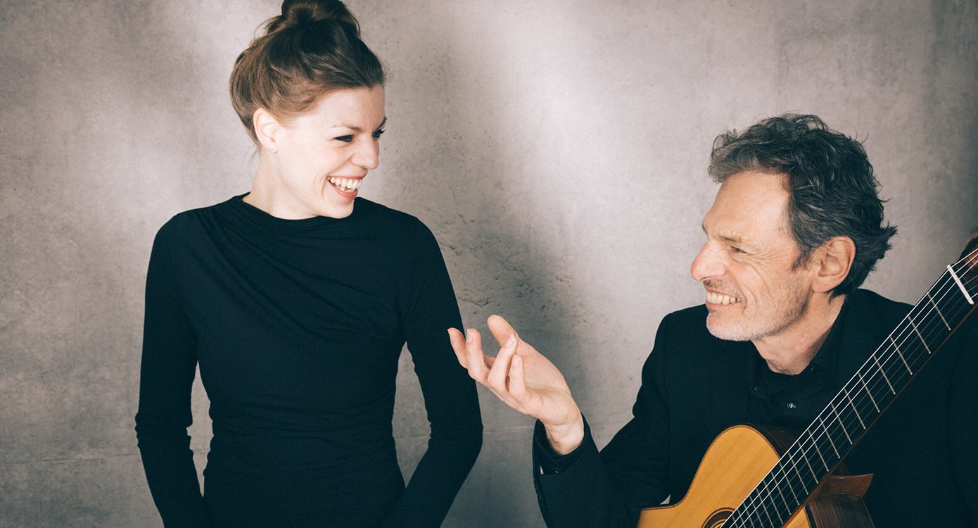 Eine Dame und ein Herr, schwarz gekleidet, er mit Gitarre in der Hand