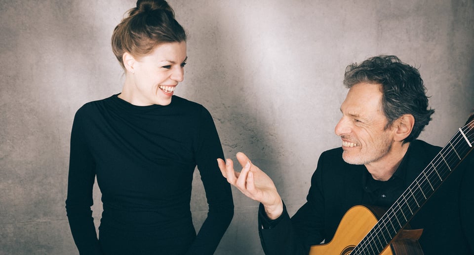 Eine Dame und ein Herr, schwarz gekleidet, er mit Gitarre in der Hand