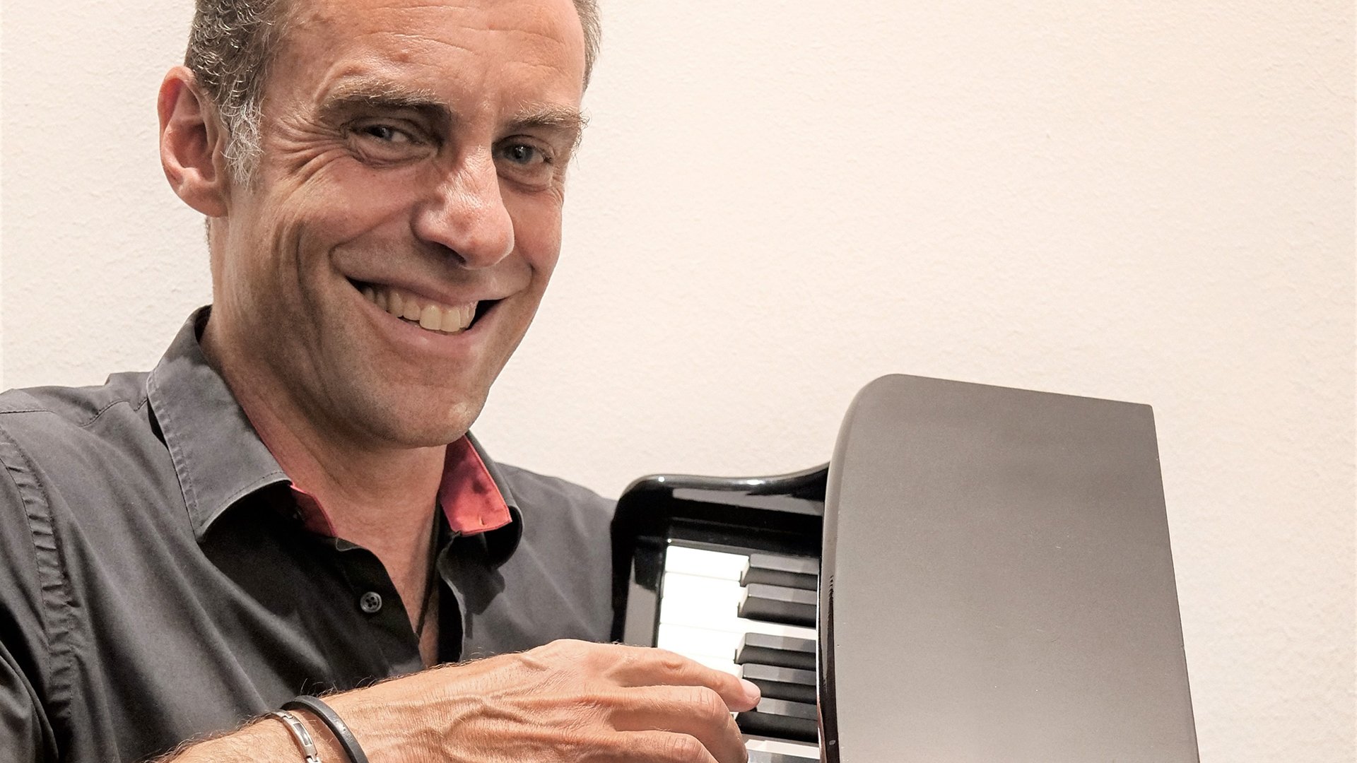 Foto für das Event „Martin Schmitt – Schmitt happens“ mit dem Künstler, der ein Klavier in den Händen hält, vor hellem Hintergrund.