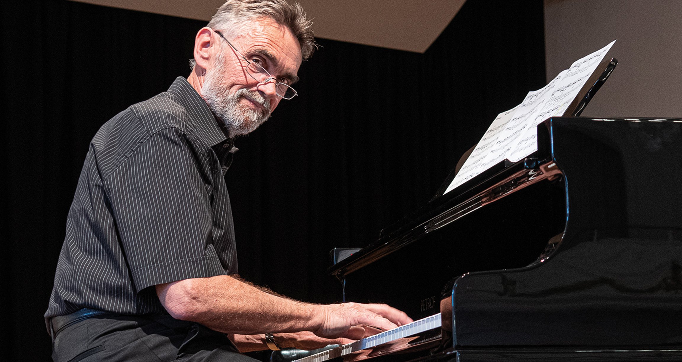 Foto eines Mannes mit Brille, der am Klavier sitzt.