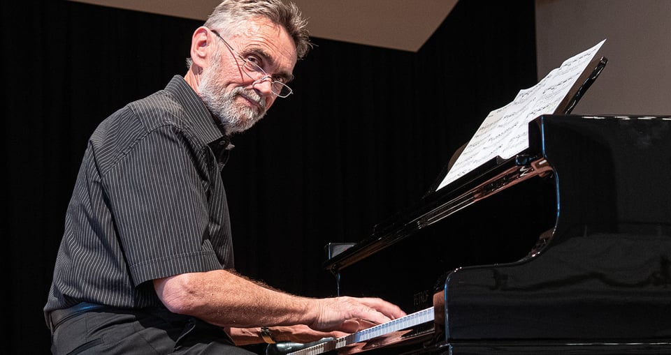 Foto eines Mannes mit Brille, der am Klavier sitzt.