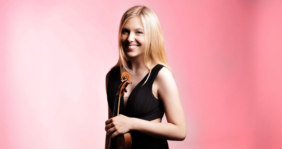 Blonde Künstlerin in schwarzer Kleidung mit Instrument vor roas Hintergrund