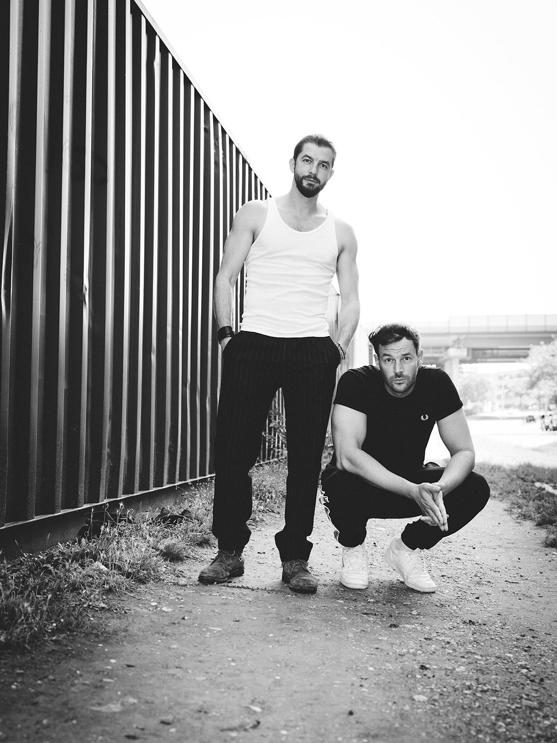 Die zwei Künstler schauen frotal in die Kamera, einer in der Hocke, der andere steht.