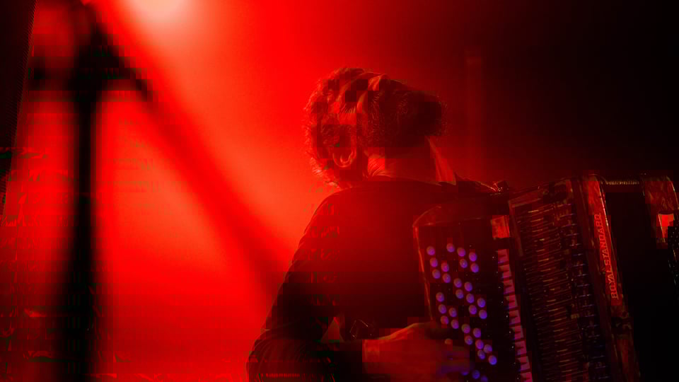 Der Künstler mit Akkordeon auf der Bühne in rotem Scheinwerferlicht