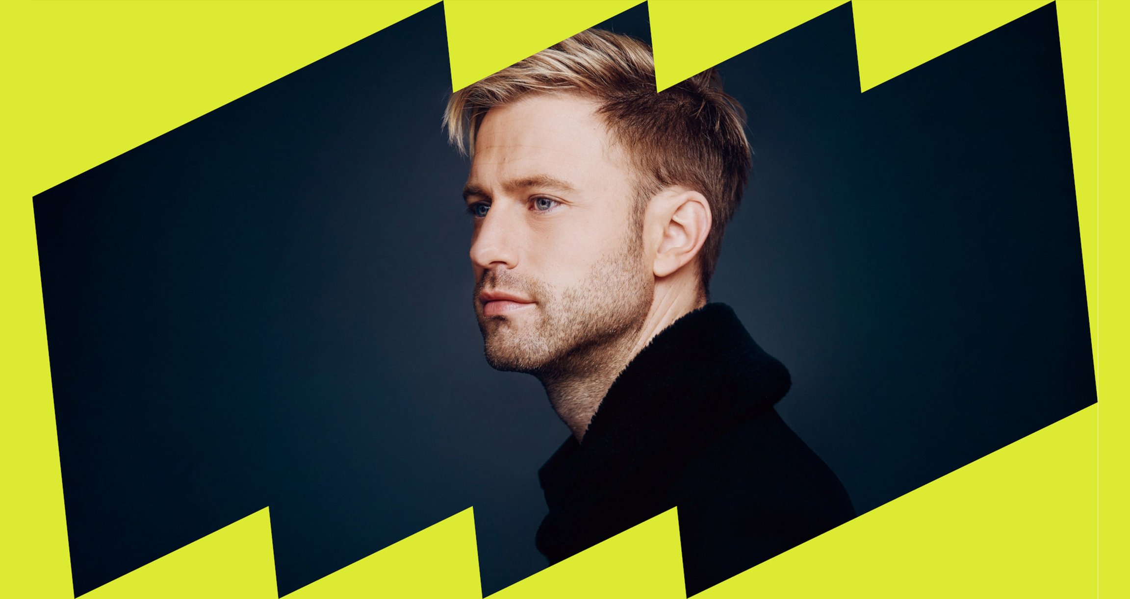 Portrait von jungem Mann mit blonden Haaren in schwarzem Pullover vor gelber Grafik