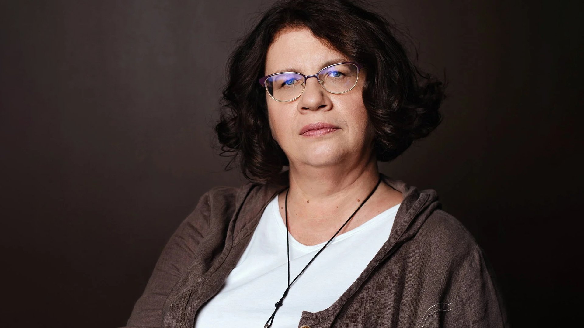 Eine Dame mit braunen Haaren und Brille vor dunkelbraunem Hintergrund