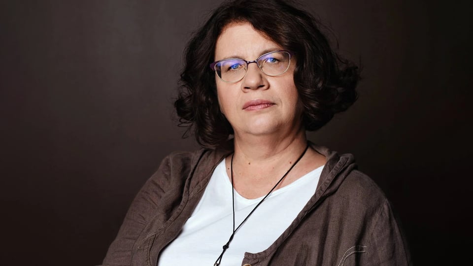 Eine Dame mit braunen Haaren und Brille vor dunkelbraunem Hintergrund