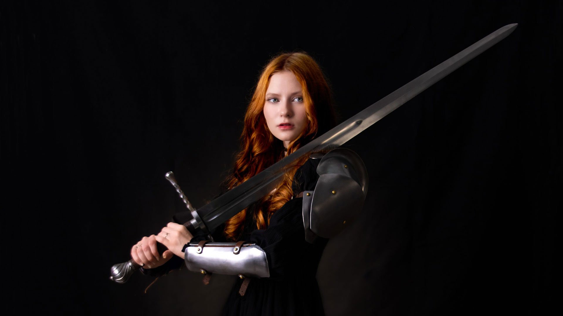 Foto von Lilith Max als Ritterin gekleidet vor dunklem Hintergrund.