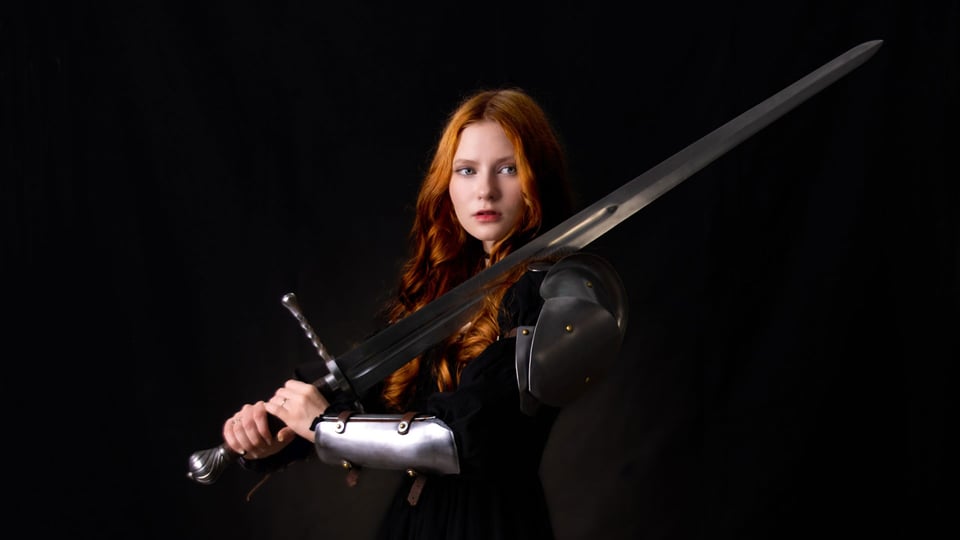 Foto von Lilith Max als Ritterin gekleidet vor dunklem Hintergrund.