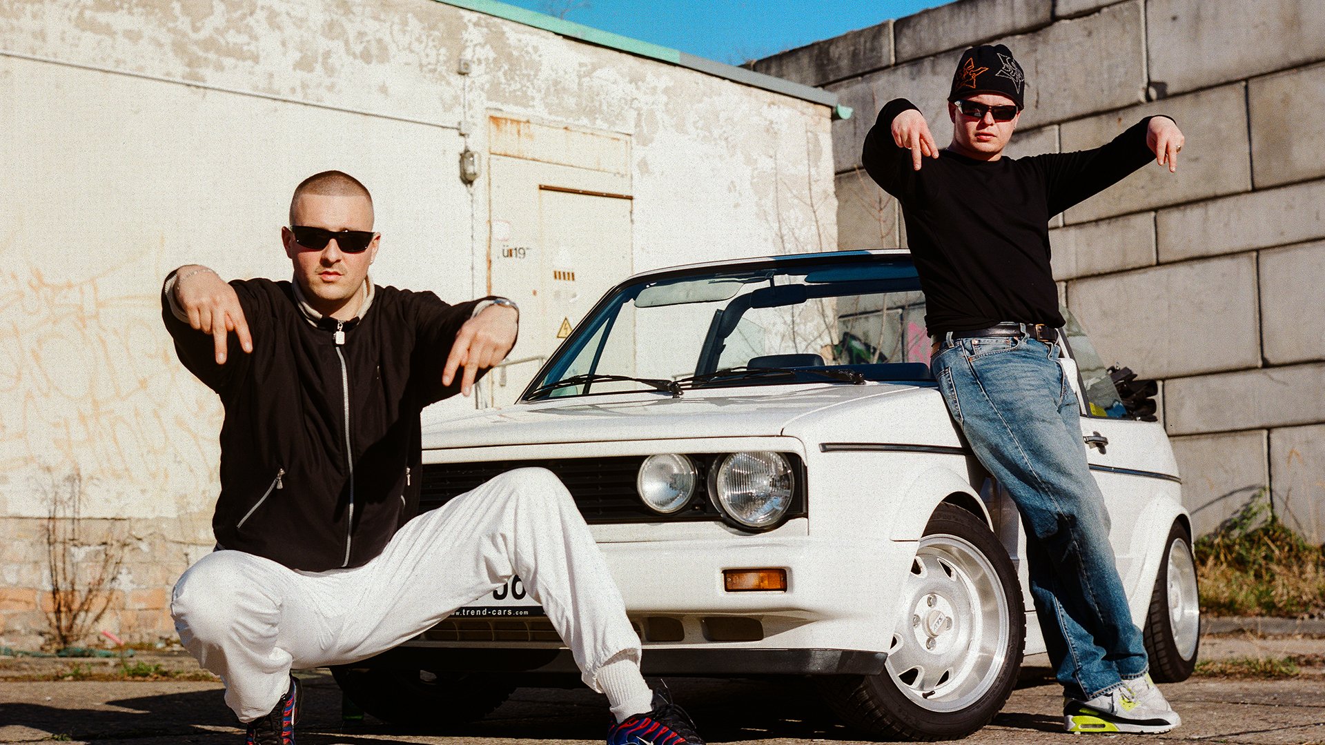 Zwei Männer posieren vor einem weißen Auto
