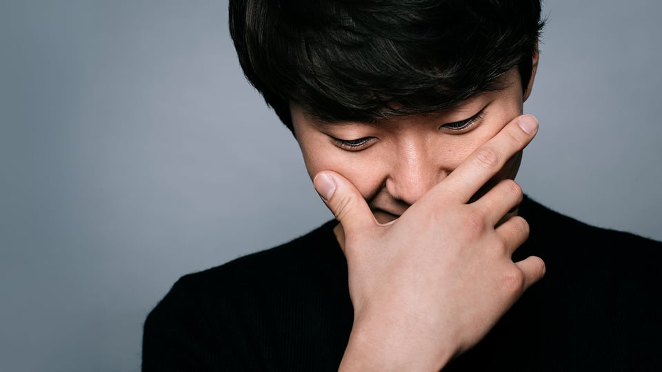 Porträtmotiv von Seong‑Jin Cho: Der Pianist ist in enger Nahaufnahme zu sehen und hält eine Hand vor das Gesicht, der Kopf ist leicht nach unten geneigt. Er trägt ein dunkles Oberteil. Neutraler grauer Studiohintergrund ohne weitere Elemente. Weiches, gerichtetes Licht betont Gesicht und Hand. Ruhiges, konzentriertes Promofoto für einen klassischen Klavierabend mit Seong‑Jin Cho.
