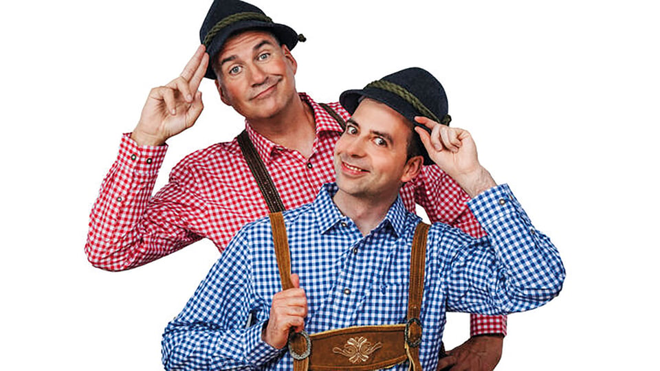 Zwei Personen in blau kariertem und rot kariertem Hemd mit braunen Lederhosen und dunklen Hüten vor hellem Hintergrund
