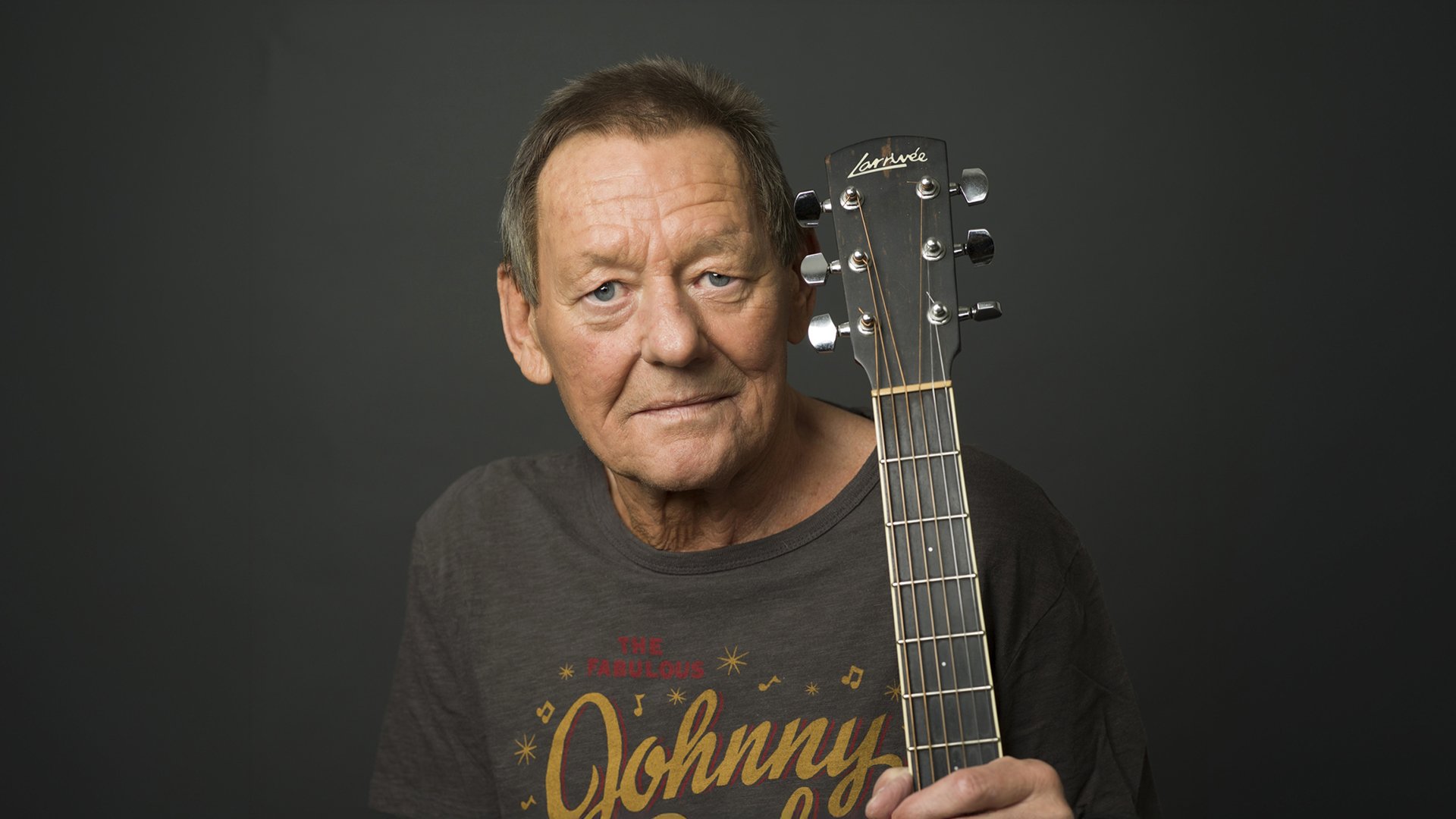 Der Künstler mit Gitarre vor dunkelgrauem Hintergrund