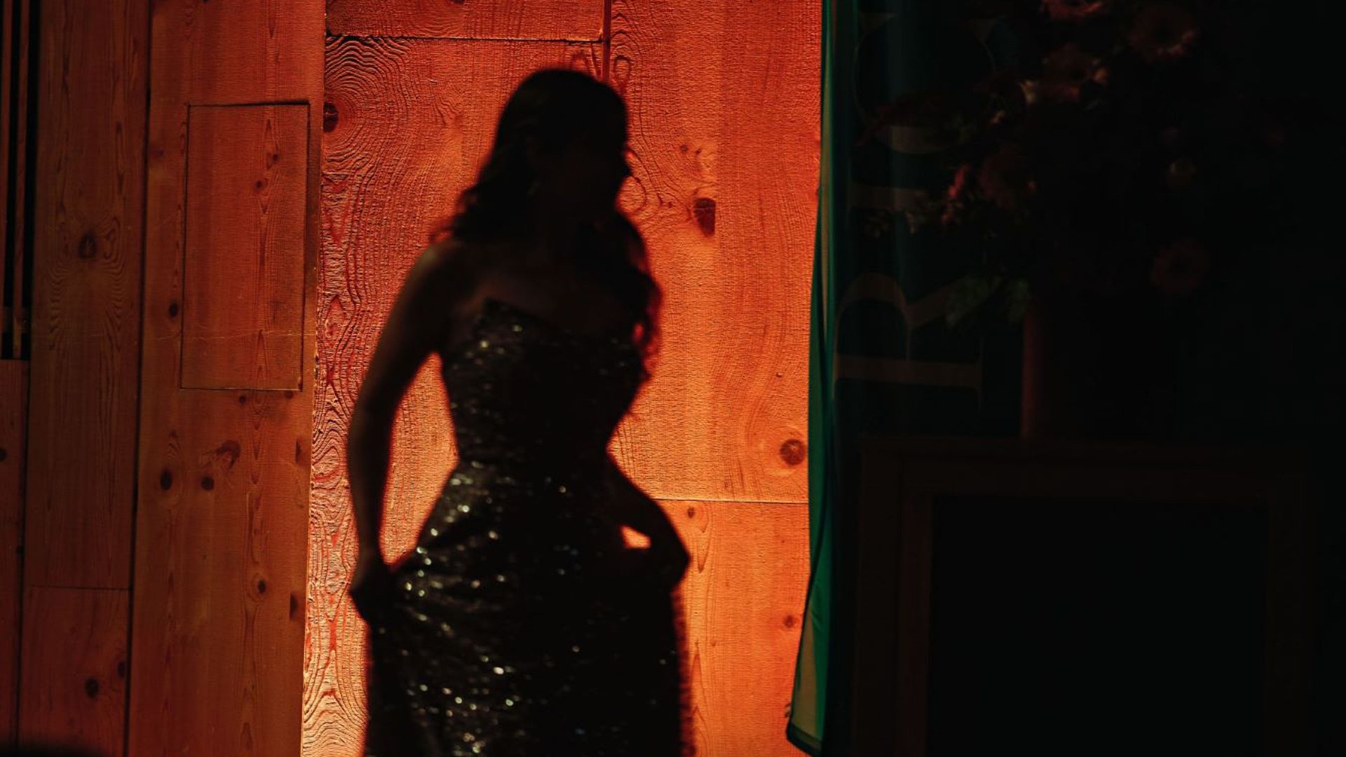 Silhouette einer Frau im eleganten Abendkleid, von warmem Bühnenlicht vor einer hölzernen Kulisse erleuchtet
