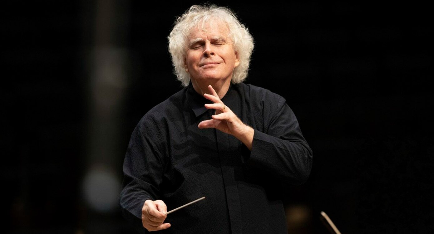Dirigent Sir Simon Rattle in schwarzem Pullover mit Dirigentenstab vor dunklem Hintergrund