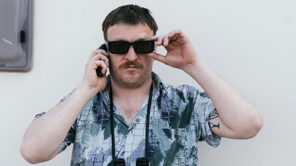 Ein Mann in gemustertem Hemd mit Sonnenbrille und Handy am Ohr