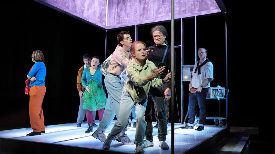 Eine Theatergruppe in bunter Freizeitkleidung auf einer Bühne mit violettem Dach