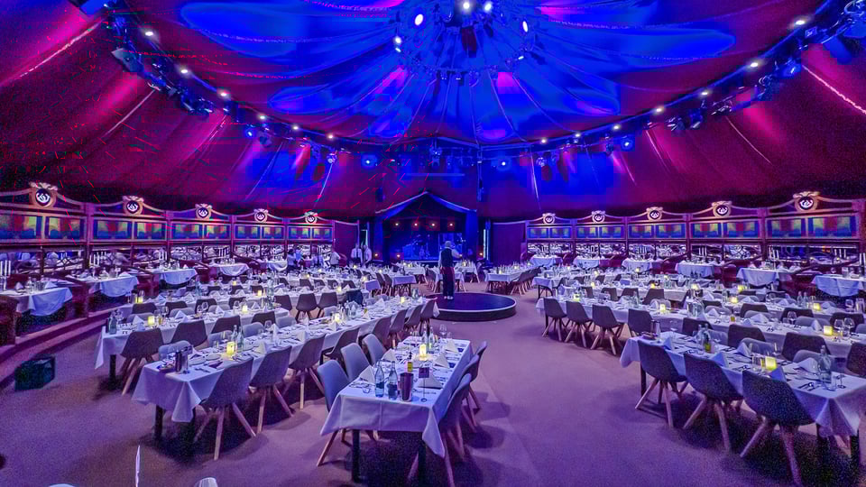 Das Zelt mit festlich gedeckten Tischen in blauem Scheinwerferlicht