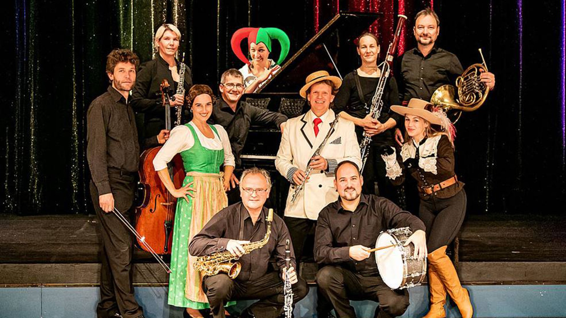 Musikergruppe auf einer Bühne mit verschiedenen Instrumenten und bunten Kostümen