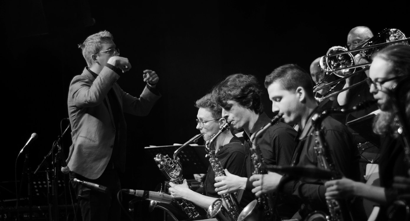 Schwarz-weiss Bild von Dirigent und Blasorchester mit Instrumenten