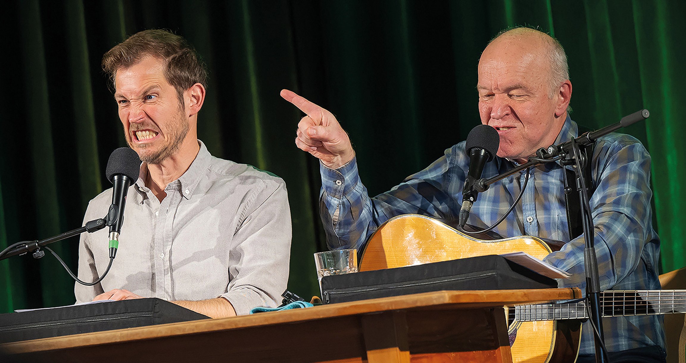 Heinz-Josef Braun und Stefan Murr am Tisch mit Mikrofon und Gitarre – offizielles Veranstaltungsbild zur musikalischen Märchenerzählung „Das Bayerische Rotkäppchen“.