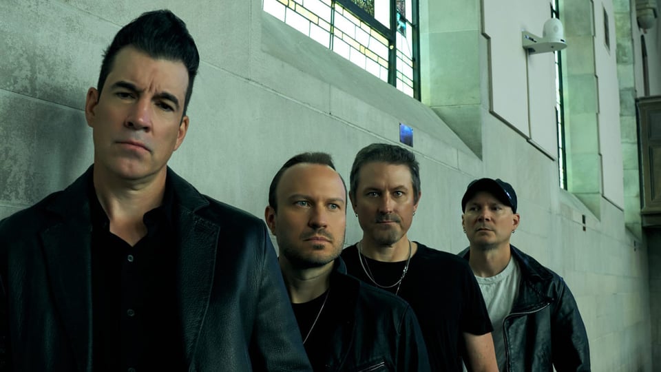 Die vier Mitglieder der Band Theory of a dead man stehen an einer Wand gelehnt, oben große Fenster