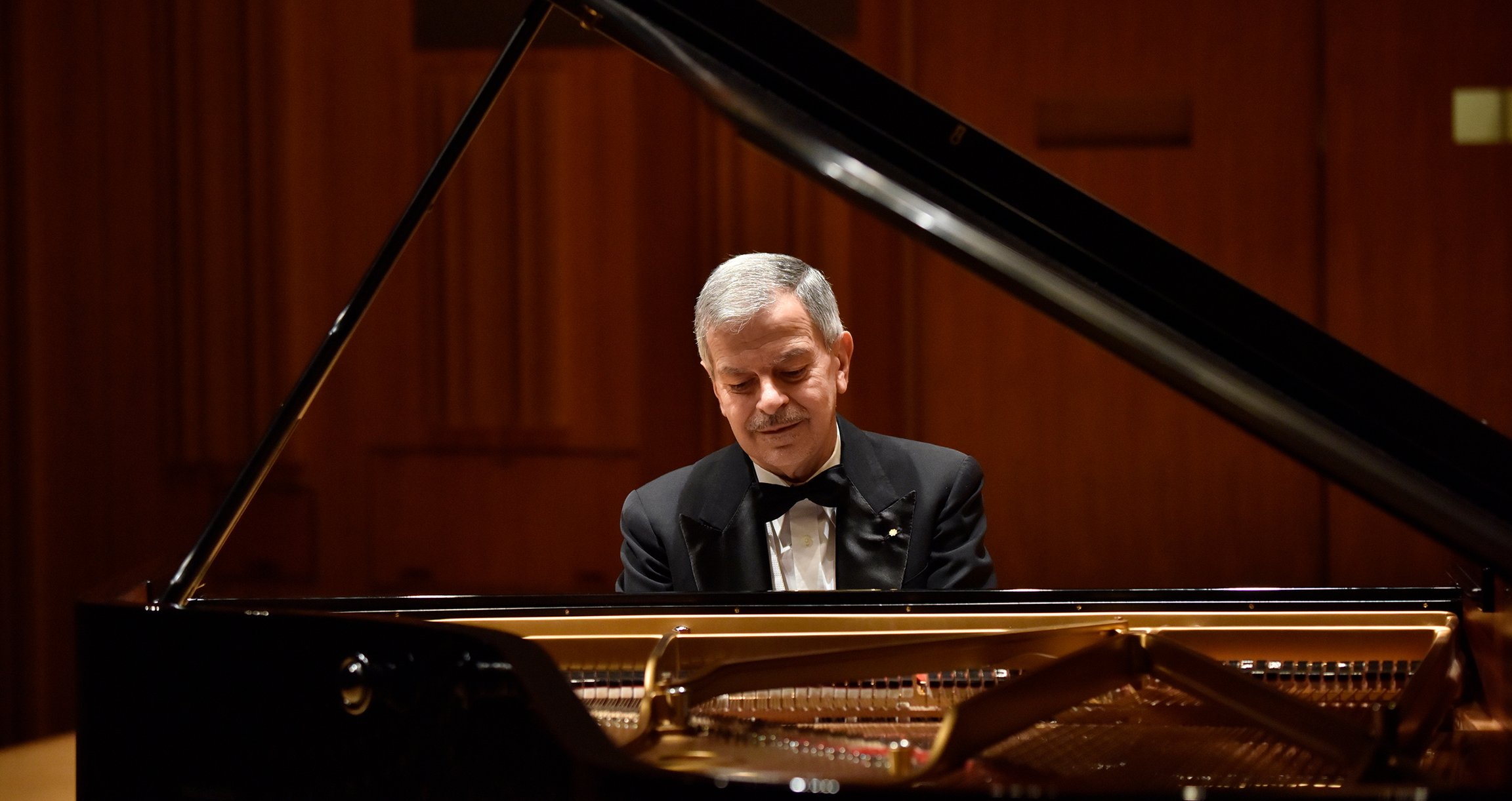Ein älterer Mann sitzt konzentriert an einem großen Flügel und spielt Klavier.