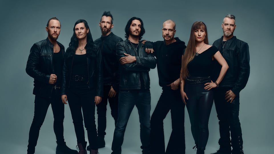 Die siebenköpfige Band in dunkler Kleidung vor grauem Hintergrund