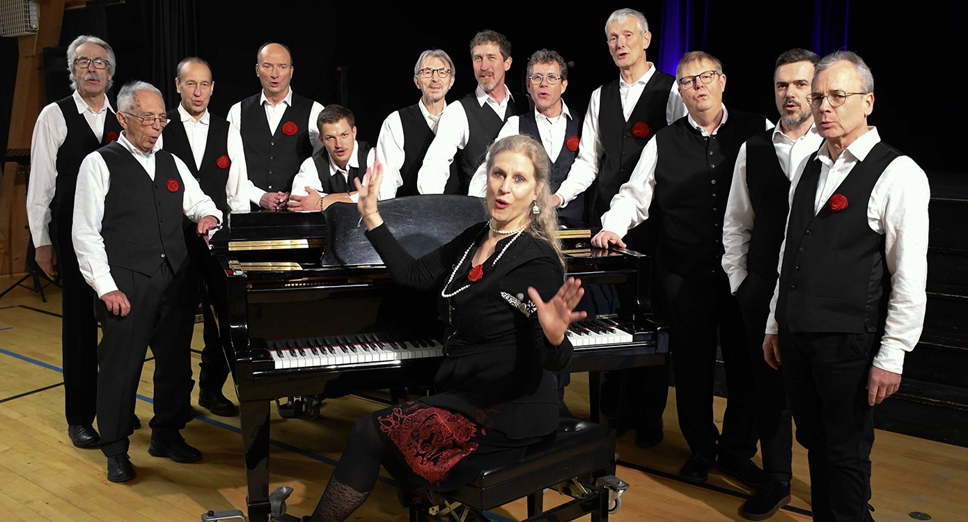 Foto einer Frau, die am Klavier sitzt, umgeben von einer Gruppe von Männern.